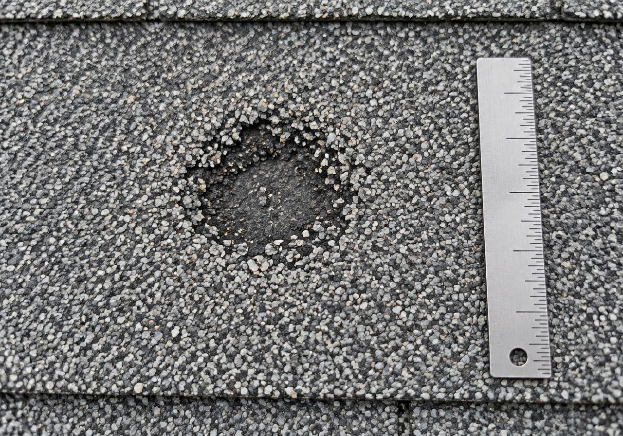 AI-generated training illustration of an impact-like spot, not a verified hail-damaged shingle. The ruler and mark are illustrative, not measurements or claim evidence.